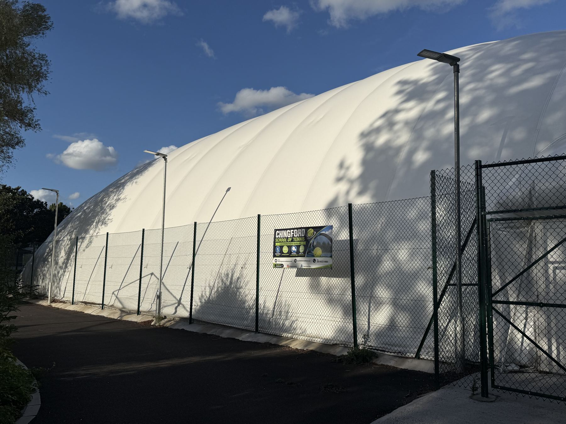 Side elevation of the permanent air dome with the Chingford School of Tennis banner on the perimeter fence