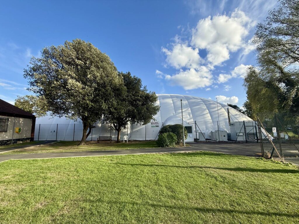 The permanent air dome at Chingford School of Tennis seen across the grass, with the clubhouse alongside