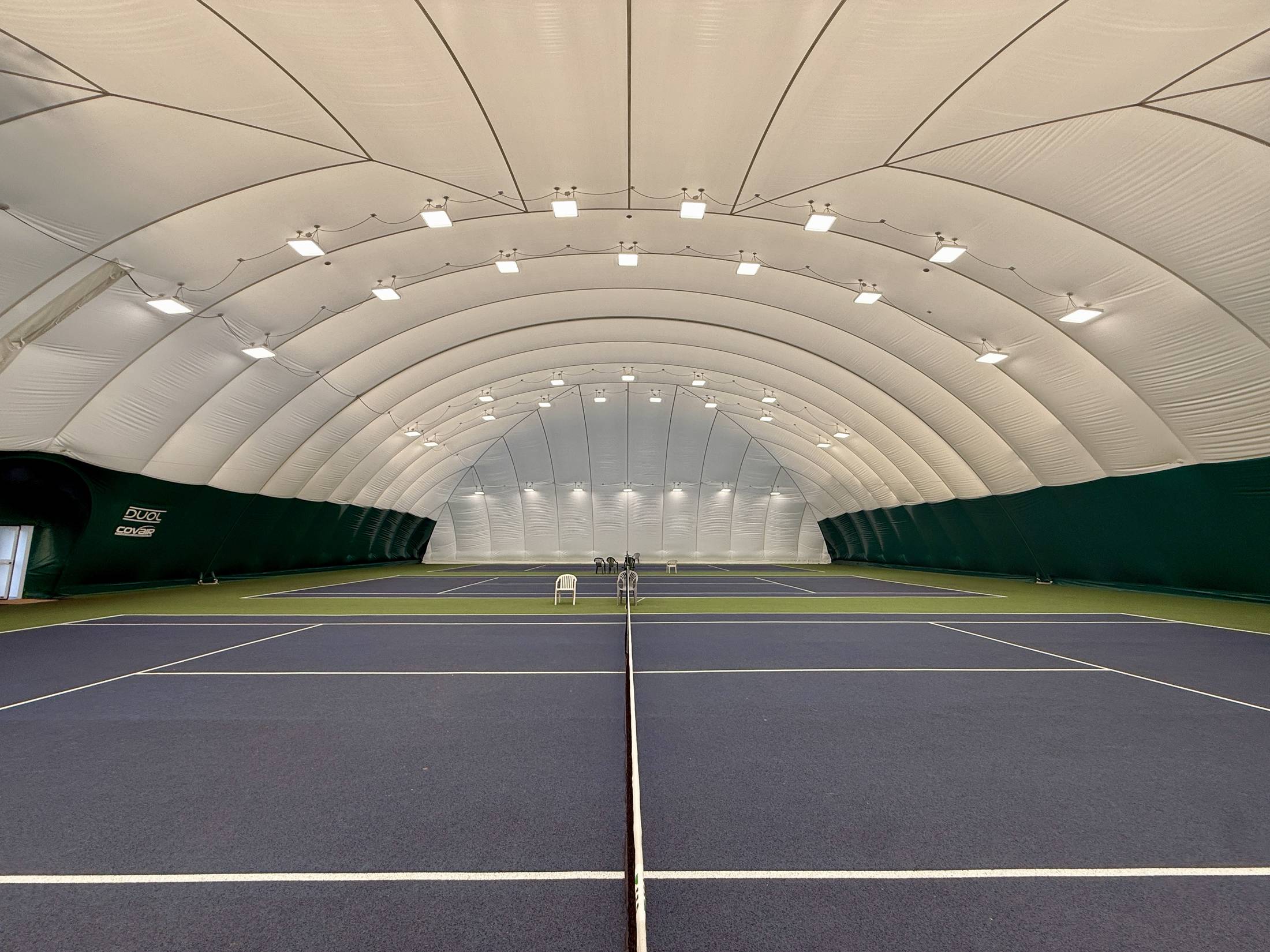 Inside the new DUOL permanent air dome at Chingford School of Tennis, looking the full length of the indoor courts under the lighting rig